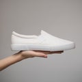 Woman`s hand holds one white sneaker. Gray background Royalty Free Stock Photo