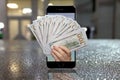 A woman`s hand holds out hundred-dollar bills from a mobile phone, a blurry urban background, raindrops. Concept: transfer money t Royalty Free Stock Photo