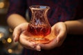 A woman\'s hand holds a pear shaped glass brimming with the rich, red goodness of Turkish tea