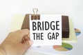 Woman s hand holds a piece of paper with text Bridge The Gap on the background of graphs and notepad Royalty Free Stock Photo
