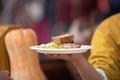 A woman`s hand holds a plastic plate with food: meat, a piece of bread and a pickle. The concept of helping the homeless and the