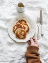 A woman\'s hand holds a plate of banana-curd pancakes - delicious breakfast, snack on a light background, top view