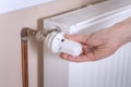 The woman`s hand holds the radiator temperature control valve and sets the required value. White radiator and copper water pipes o