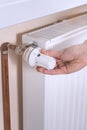 The woman`s hand holds the radiator temperature control valve and sets the required value. White radiator and copper water pipes o