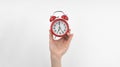 A woman\'s hand holds a red alarm clock against a white wall