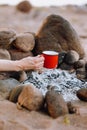 a woman's hand holds a red cup of coffee or tea against the background of a campfire on a hike. hiking and outdoor Royalty Free Stock Photo