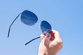 Woman`s hand holds sunglasses against the sky, the glasses of which reflect the azure sea Royalty Free Stock Photo