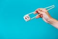 Woman`s hand holds Tasty sushi roll maki with wooden chopsticks on blue background close up. Place for caption and text Royalty Free Stock Photo