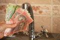Woman`s hand holds a Ukrainian 10 20 hryvnia near the kitchen tap, water prices Royalty Free Stock Photo