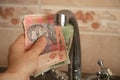 A woman`s hand holds a Ukrainian 10 20 hryvnia near the kitchen tap Royalty Free Stock Photo