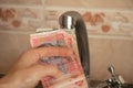 A woman`s hand holds a Ukrainian 10 20 hryvnia near the kitchen tap Royalty Free Stock Photo