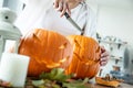 Woman`s hand with knife cuts pumpkin for Halloween