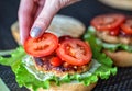 A woman& x27;s hand lays down a slice of tomato on a delicious homemade burger. Handmade homemade burgers, close-up