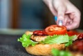 A woman`s hand lays down a slice of tomato on a delicious homemade burger. Handmade homemade burgers, close-up