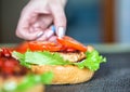 A woman`s hand lays down a slice of tomato on a delicious homemade burger. Handmade homemade burgers, close-up