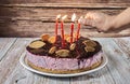 Woman`s hand lighting candles on a forest fruit mousse cake decorated with pieces of biscuit, on a wooden background. Selective