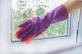 Woman`s hand in a lilac rubber glove wipes a glass unit window in a room with a rag