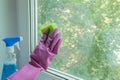 Woman`s hand in a lilac rubber glove wipes a glass unit window in a room with a sponge