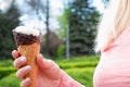 A woman's hand with a manicure holds a chocolate waffle cone of ice cream on the background of a green nature park