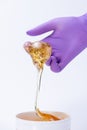 Woman`s hand in a glove holds yellow sugar paste or wax for depilation close up on a white background