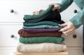 Woman`s hand organizing stack of warm wool and cotton clothes. Winter autumn wardrobe concept