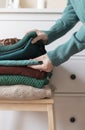 Woman`s hand organizing stack of warm wool and cotton clothes. Winter autumn wardrobe concept