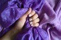 A woman`s hand with pale lilac nails holds a purple silk fabric against a background of lilac cotton fabric Royalty Free Stock Photo