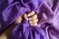 A woman`s hand with pale lilac nails holds a purple silk fabric against a background of lilac cotton fabric Royalty Free Stock Photo