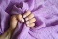 A woman`s hand with pale purple painted nails holds a lilac cotton fabric on a lilac fabric background Royalty Free Stock Photo