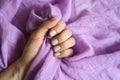 A woman`s hand with pale purple painted nails holds a lilac cotton fabric on a lilac fabric background Royalty Free Stock Photo