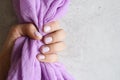 A woman`s hand with pale purple painted nails holds a lilac cotton fabric on a gray concrete background. space for text Royalty Free Stock Photo