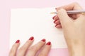 Woman`s hand with pen in position to write on blank white paper on a pink background Royalty Free Stock Photo