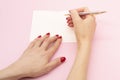 Woman`s hand with pen in position to write on blank white paper on a pink background Royalty Free Stock Photo