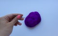 Woman`s hand with pink manicure holding the steel needle above piece of violet wool on white background. Concept of felting creati