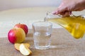A woman& x27;s hand pours apple cider vinegar in a glass bottle on a light background into a glass of water. Malic acid is