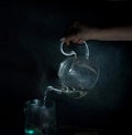 Woman`s hand pours boiling water into a glass kettle. dark background. vintage.