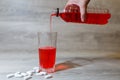 A woman's hand pours a red sports drink or lemonade into a glass Cup from a plastic bottle. Energy drink in glass and plastic bot