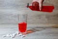 A woman's hand pours a red sports drink or lemonade into a glass Cup from a plastic bottle. Energy drink in glass and plastic bot