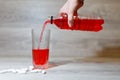 A woman's hand pours a red sports drink or lemonade into a glass Cup from a plastic bottle. Energy drink in glass and plastic bot