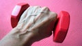 A woman`s hand pressing a red dumbbell against a bright red background.