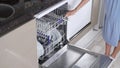 A woman's hand pushes out the empty top shelf of a housewife's dishwasher close-up