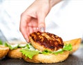A woman& x27;s hand puts a juicy beef cutlet on a burger bun. Making burgers at home, close-up