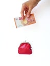 A woman`s hand puts money in a red purse with a metal lock on a white background. Saving money. Royalty Free Stock Photo