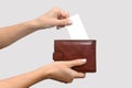 A woman& x27;s hand puts a white business card into a leather purse. On a gray background. Royalty Free Stock Photo