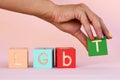 A woman`s hand with rainbow nails lays out the inscription LGBT from cubes. abbreviation LGBT on a pink background.