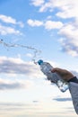 A woman`s hand raises a highly transparent bottle of pure mineral water. Splashes are flying against the background of a blue sky Royalty Free Stock Photo