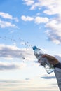 A woman`s hand raises a highly transparent bottle of pure mineral water. Splashes are flying against the background of a blue sky Royalty Free Stock Photo