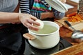 Woman`s hand with raw onion to put it into the boiling water. Opened white saucepan on the black stove. Cooking a soup Royalty Free Stock Photo