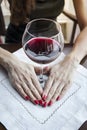 A woman`s hand with a red nail holds a goblet with red wine, large glass of red wine on a white napkin on the table in