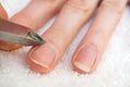 Woman`s hand removing nail cuticle on light white table. Care about dry, overgrown cuticle. Closeup.